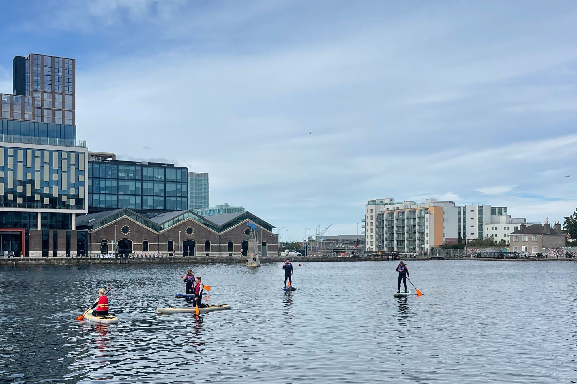 People paddleboarding on a body of water with buildings in the background