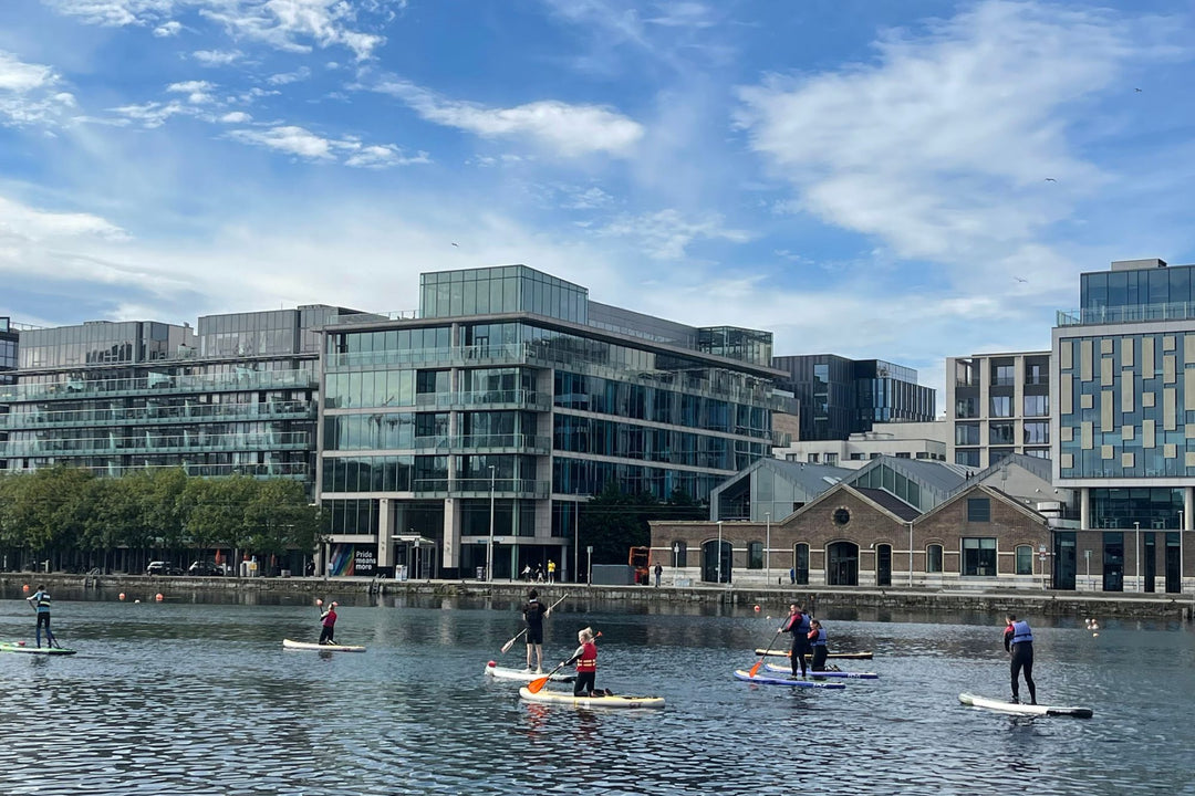 People paddleboarding on a body of water with modern buildings in the background