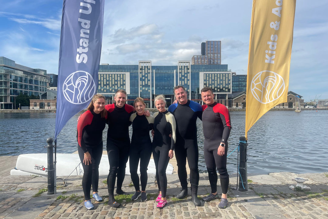 Group of people in wetsuits standing by a waterfront with flags in the background