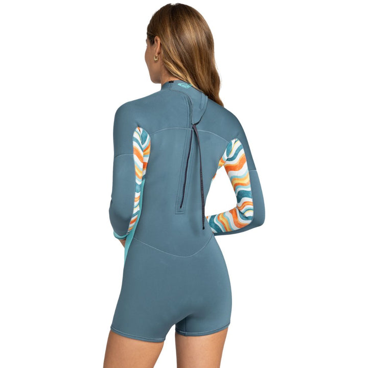 Studio photo of model wearing Roxy Swell Series Womens Shorty Wetsuit with long sleeves and back zip. Back view. 