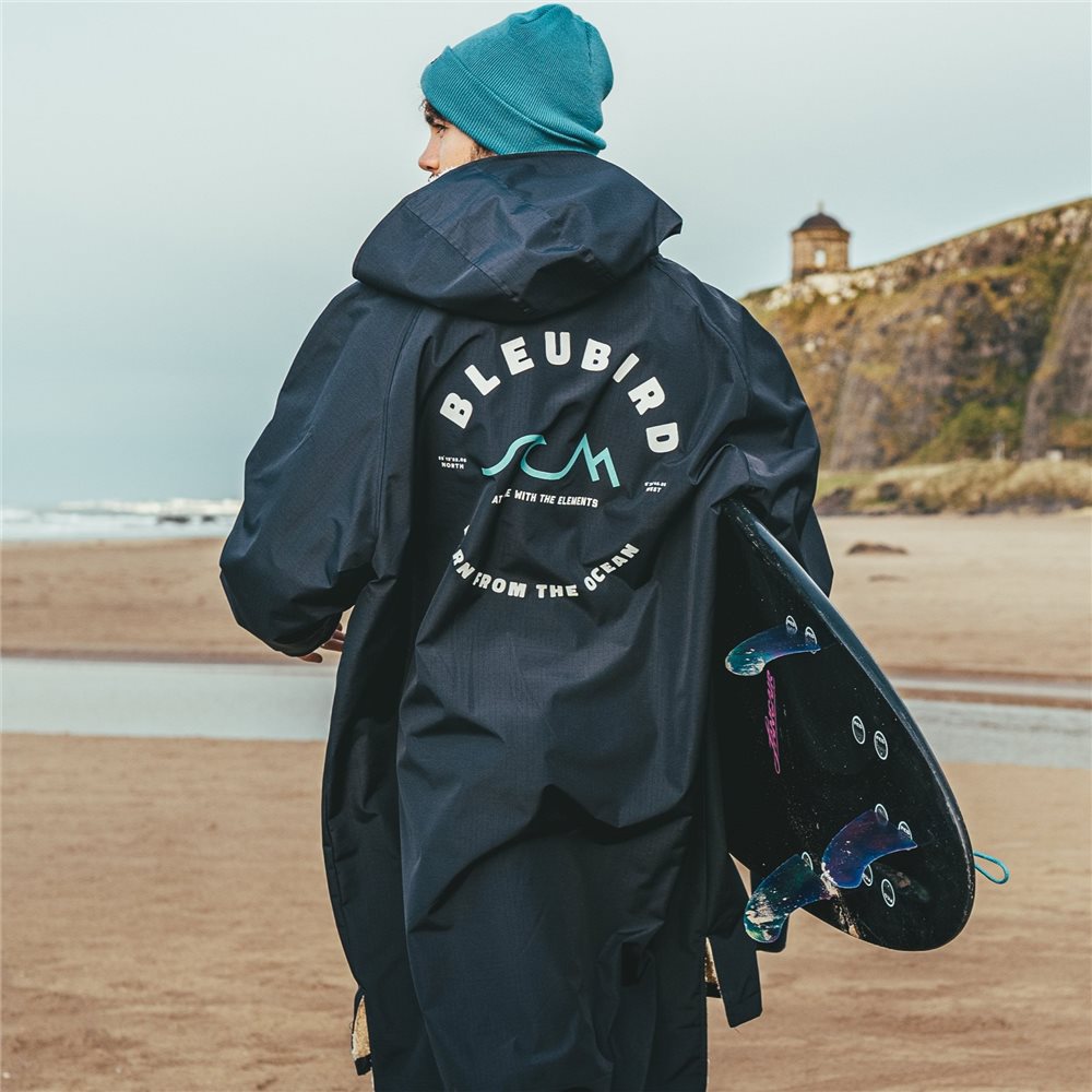 A man wearing a long-sleeved navy-colored Bleubird Nordic outdoor changing robe with a hood
