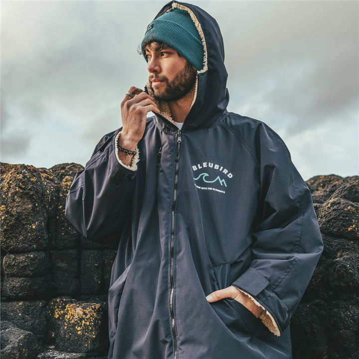 A man wearing a long-sleeved navy-colored Bleubird Nordic outdoor changing robe with a hood