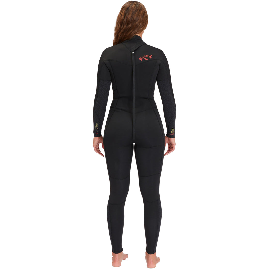 A woman standing and posing in a black full-sleeve Billabong Synergy womens wetsuit with a back zip. Show the back of the wetsuit