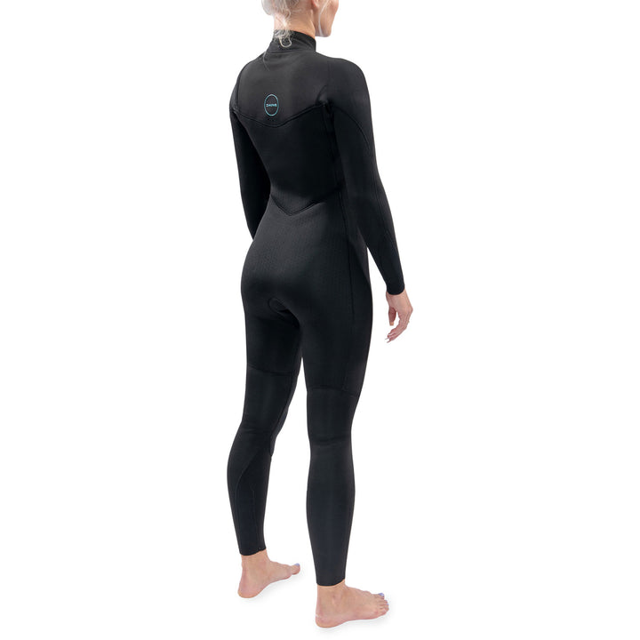 A woman standing at an angle with her back facing is wearing a black Dakine Mission chest zip womens wetsuit with blue detailing.
