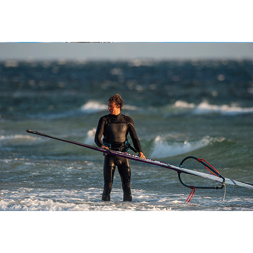 Model wearing 2020 O'Neill Mens Mutant Legend 5/4 Chest Zip Wetsuit with detachable hood holding a windsurf in the sea